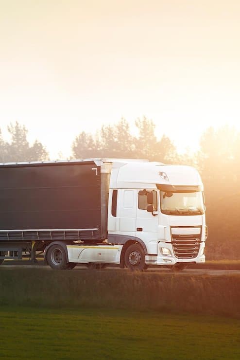 A freight truck driving along a road at sunset