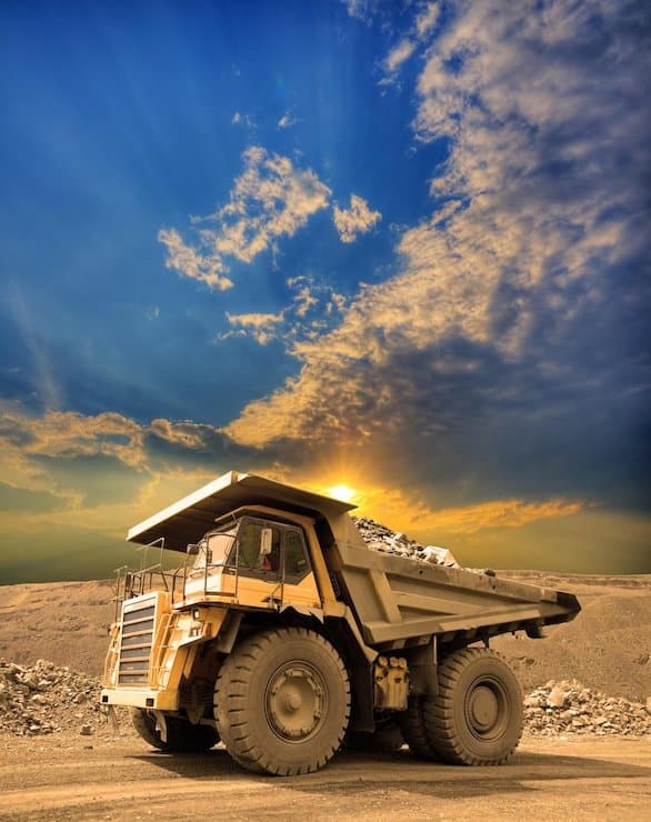 A heavy mining haul truck driving through an open-pit mine at sunset